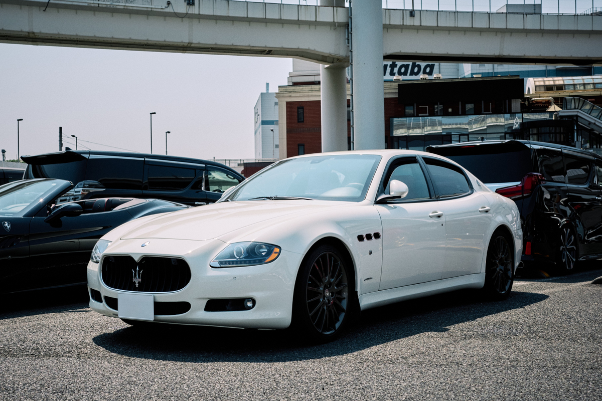 White Maserati Quattroporte parked at Daikoku Parking Area in Japan, with elevated expressway structures and a clean urban backdrop, capturing the essence of Japanese car culture.