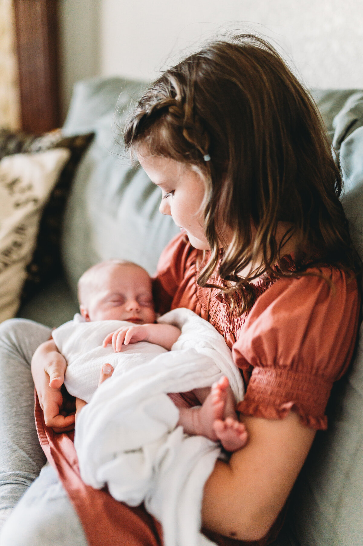 proud big sister holds new baby sister on couch at home
