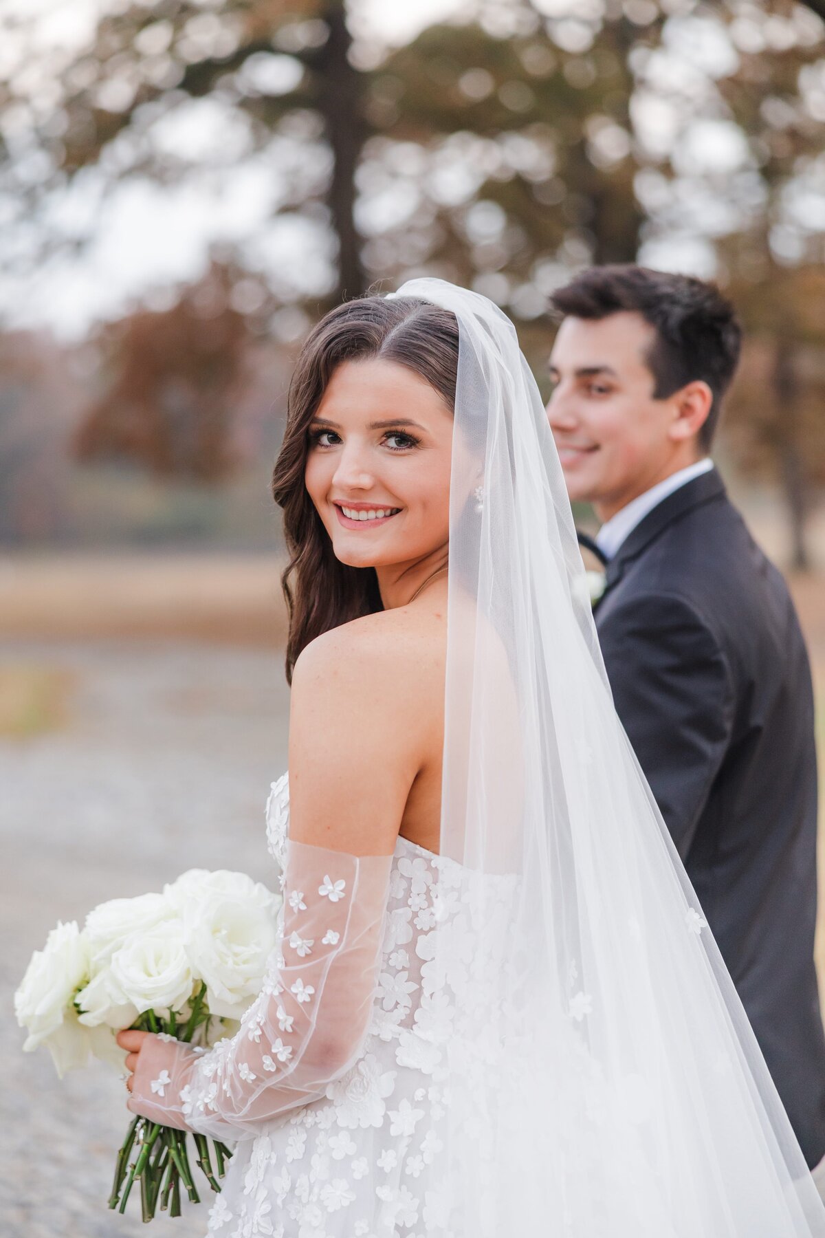 An Arkansas wedding photographer image of newlyweds walking holding hands while the bride smiles over her shoulder