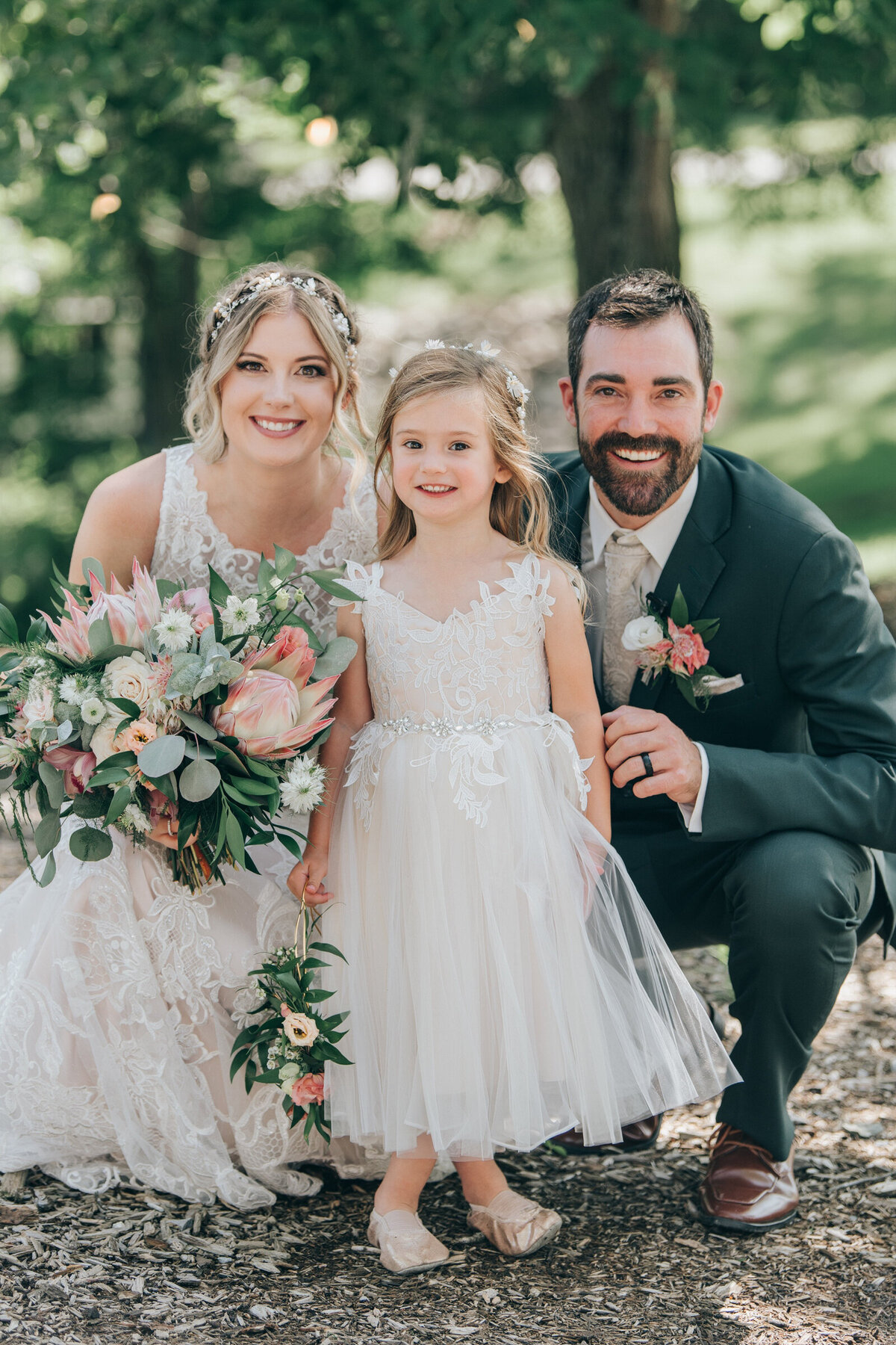Bride and groom posing with their daughter, the flower girl, on their Summer wedding day