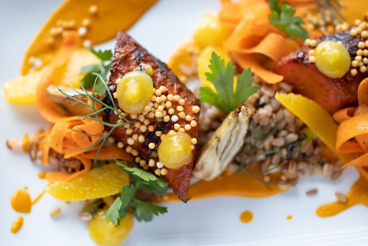 Plated dish with grilled protein, yellow sauce, and fresh herbs