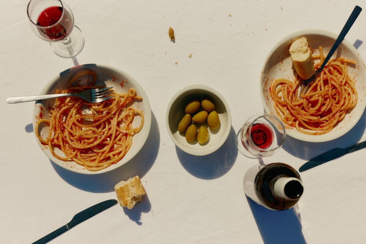 Overhead view of Italian-style pasta with red sauce served in white bowls alongside green olives, bread, and wine, representing the warm dining experience offered by Vida Foods in St. Petersburg, Florida.