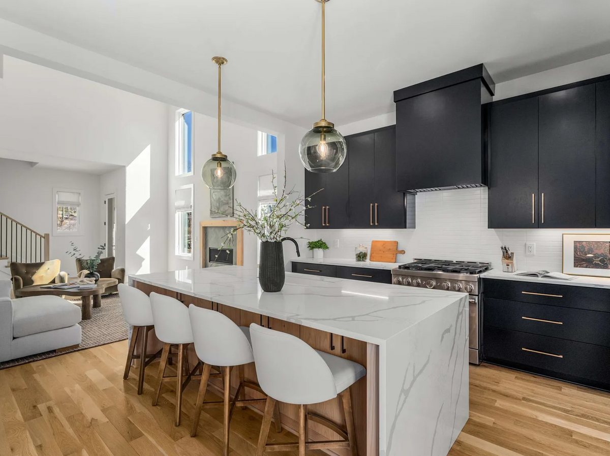 Contemporary kitchen with black cabinetry, quartz waterfall island, brass hardware, globe pendant lights, and open flow to living space