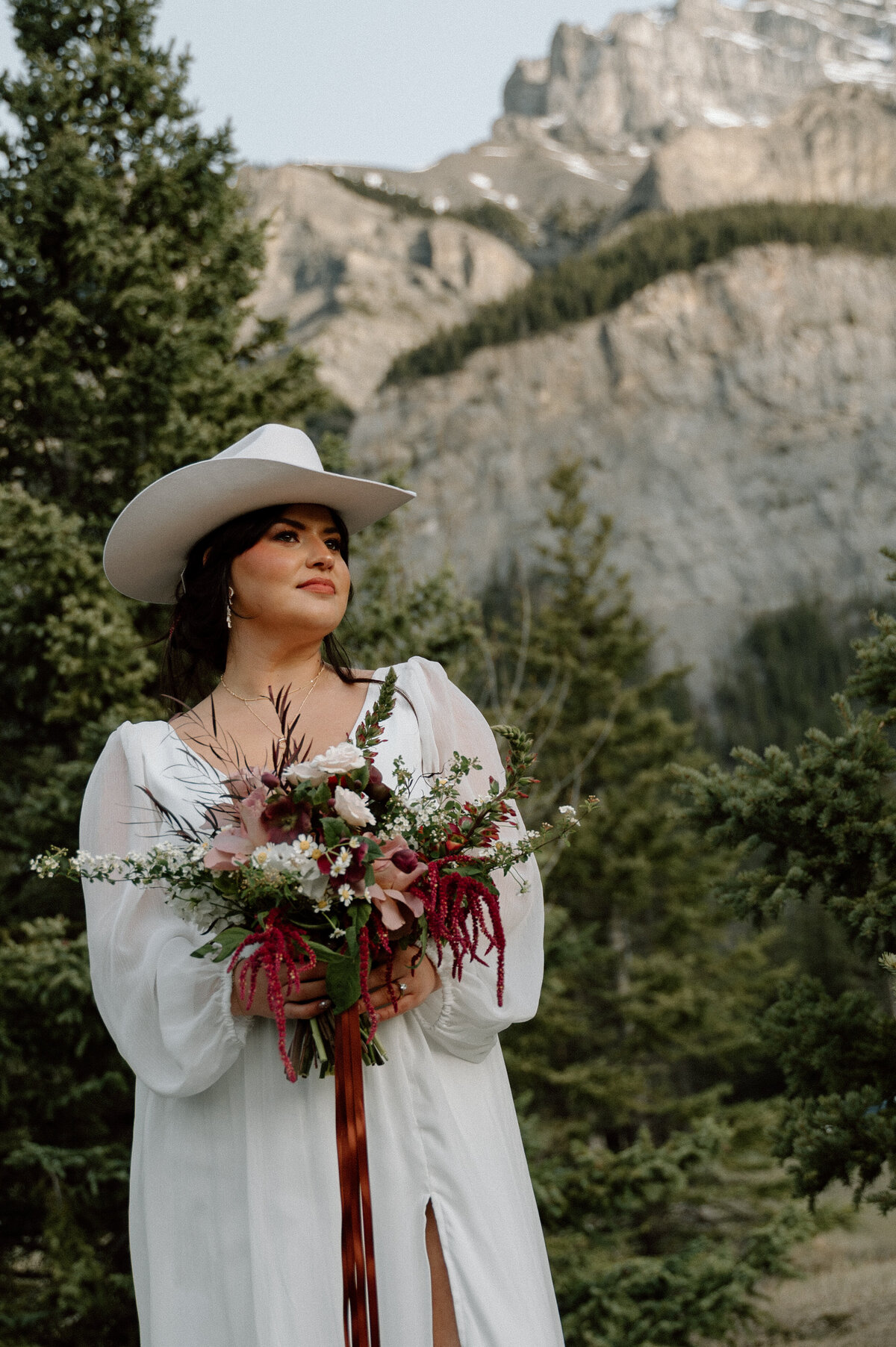 Cowgirl-inspired bride poses with rustic bouquet against Rocky Mountain backdrop in Banff.