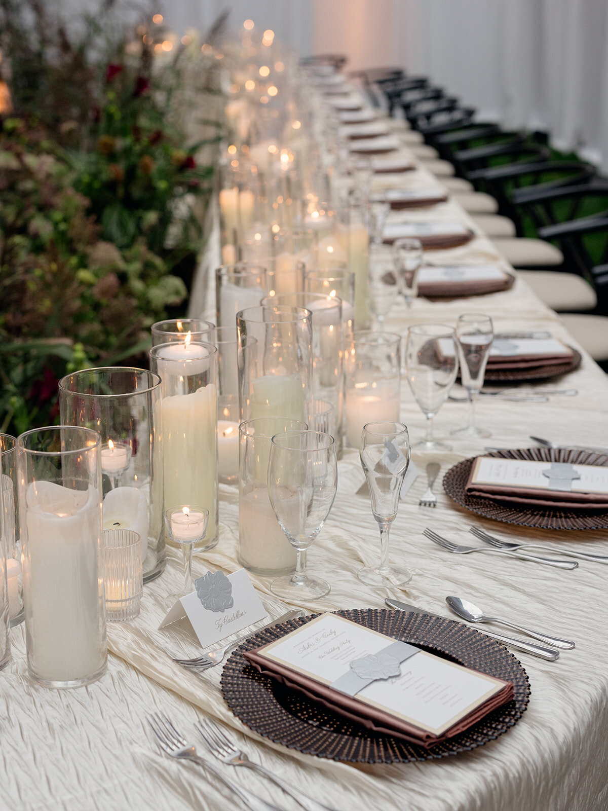 Long reception table lined with glass candle cylinders and dark charger plates