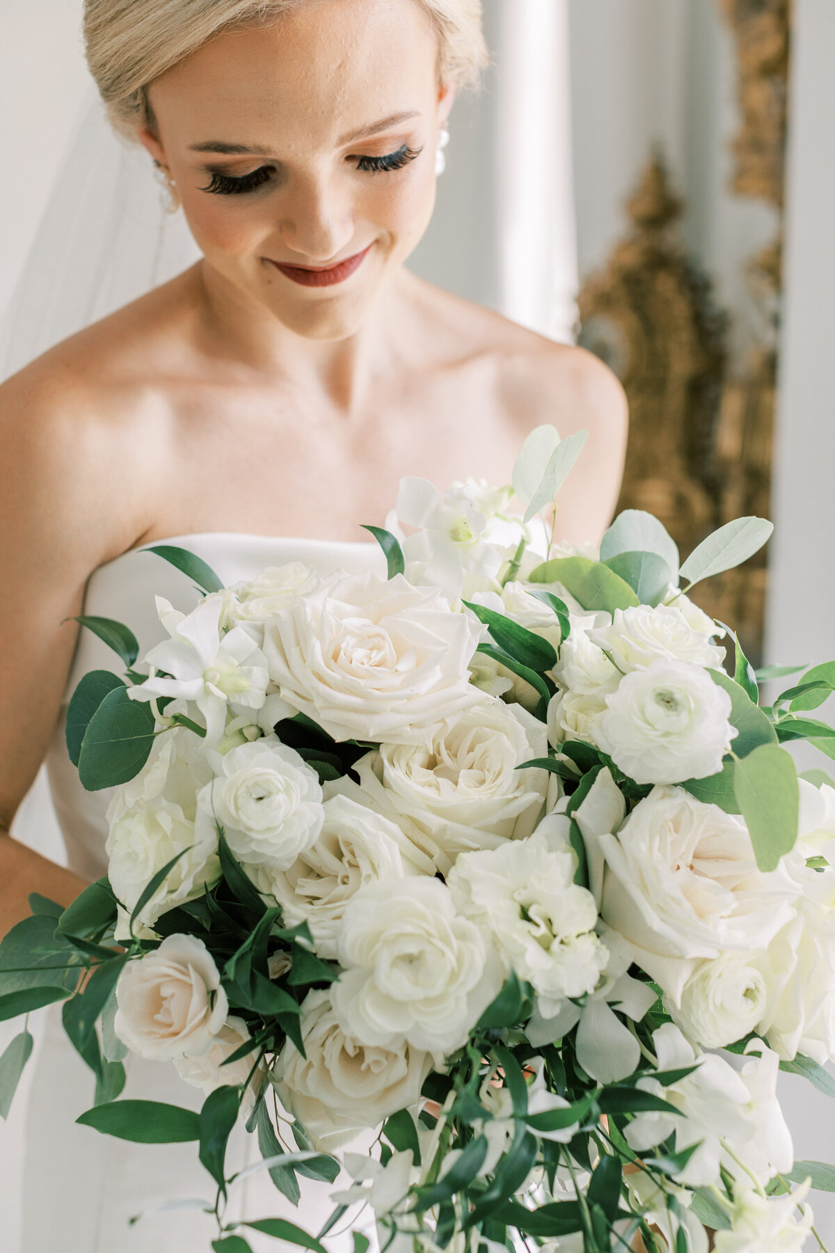 A bride looks down at her white and green bouquet.