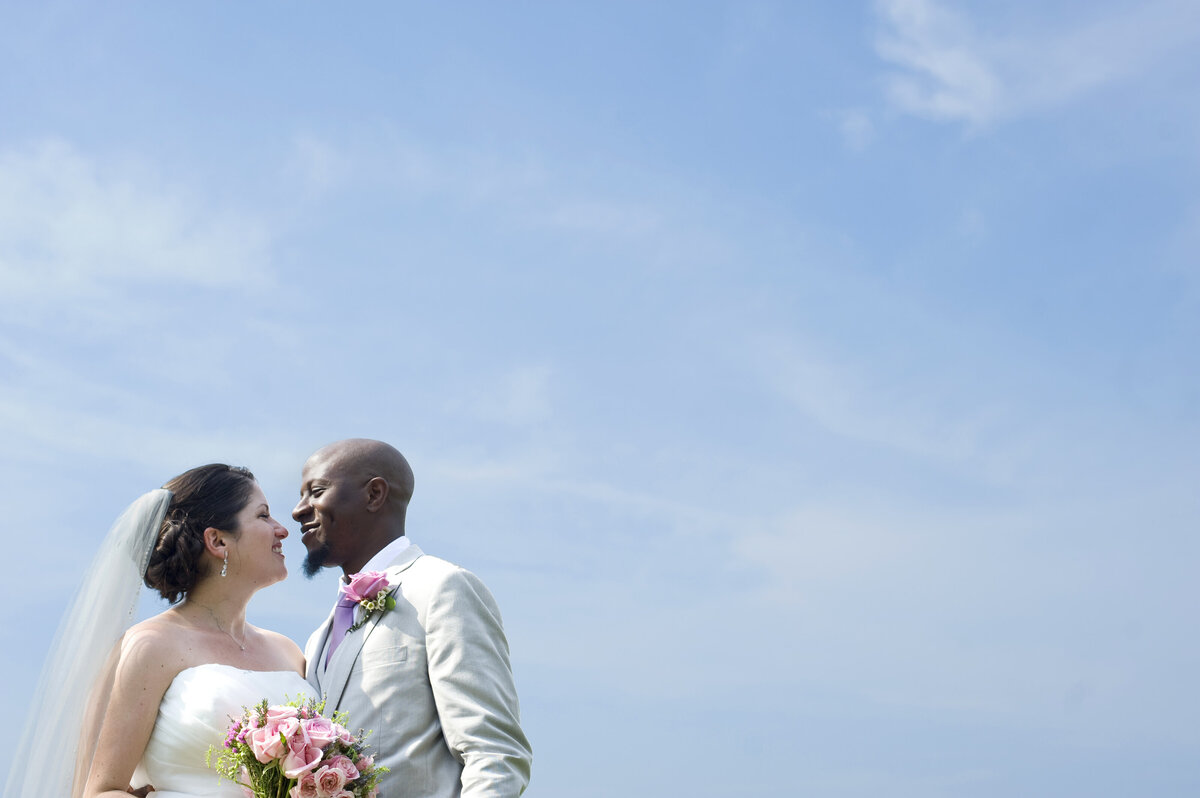 A newlywed couple standing close together and smiling at each other 
