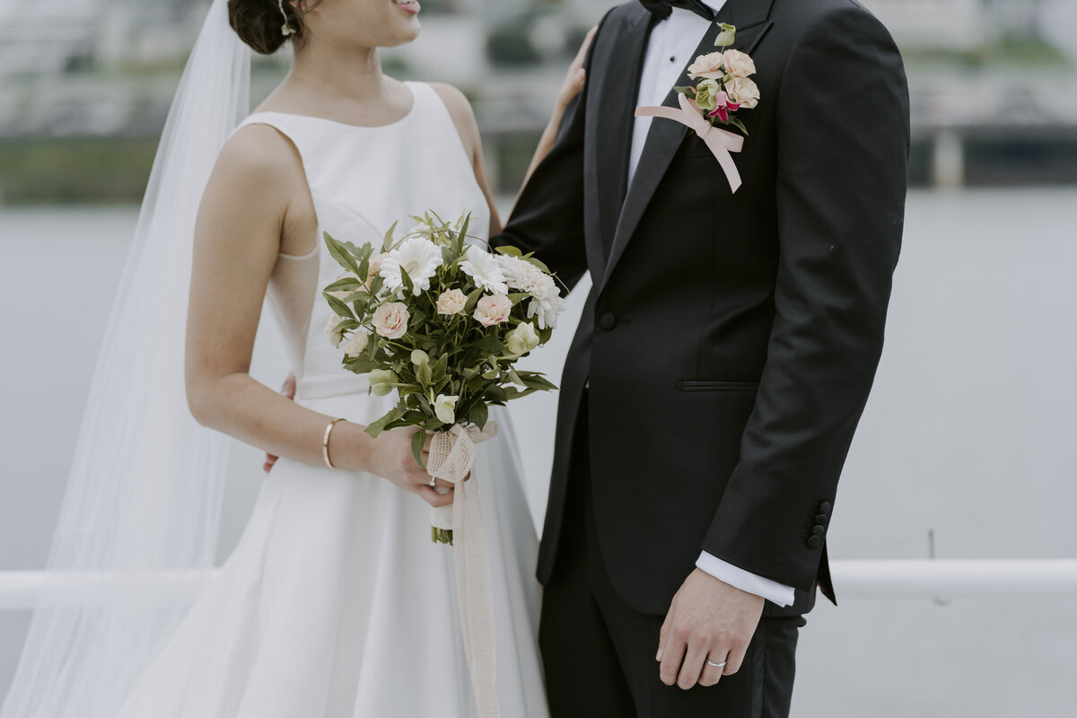bride's white dress and viel and holding her fresh flower bouquet and the groom's black suit pinned with a fresh flower and hid bowtie
