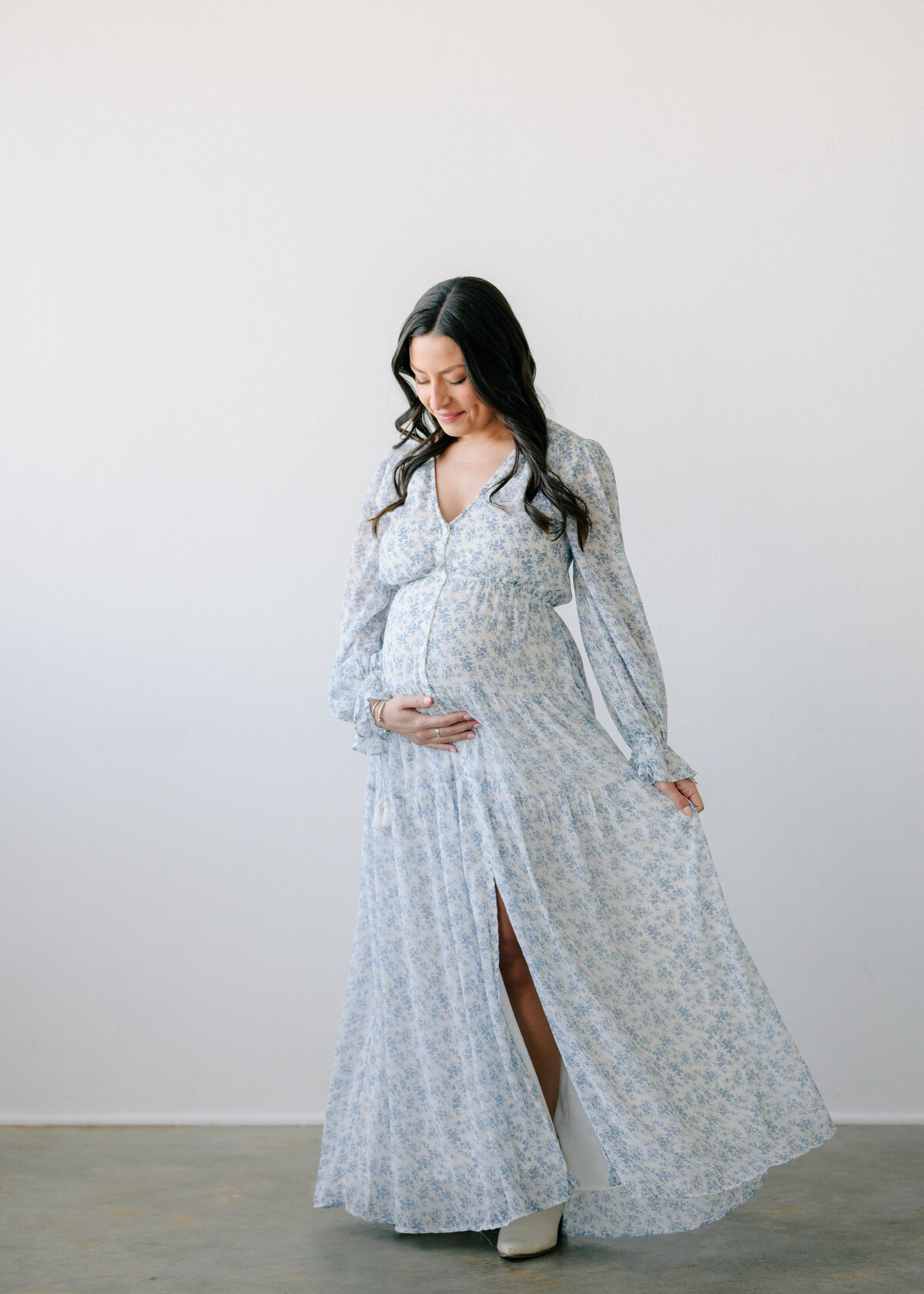 Pregnant woman in a long floral dress  and twirling while she holds her baby bump- photo by Maegan R Photography