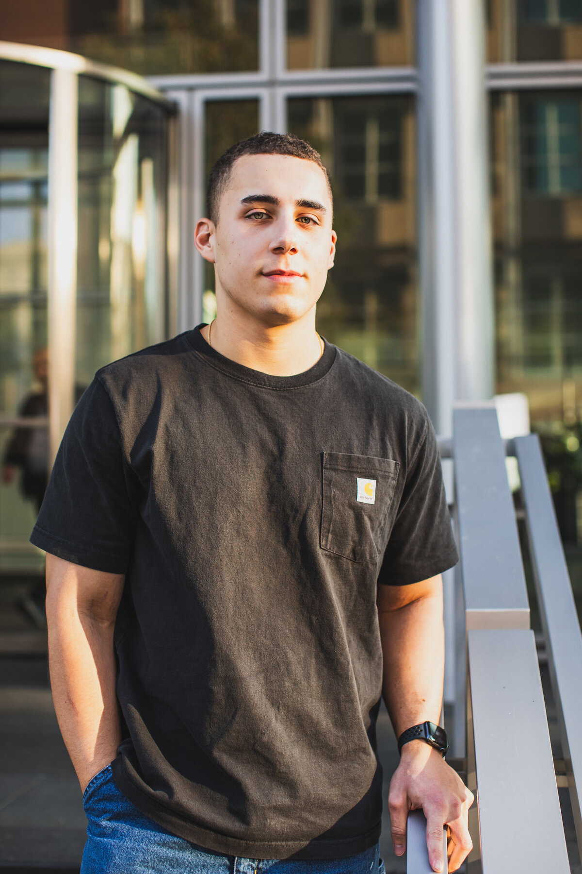 this handsome senior boy stands in front of a glass and metal building on Pittsburghs north shore for his graduation portrait.