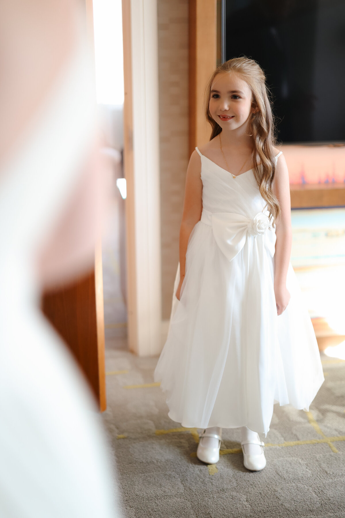 Bride sharing her first look with her family, who are smiling and cheering as they see her wedding gown for the first time in an elegant room.