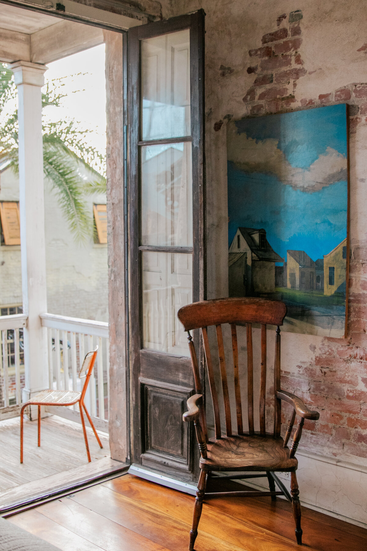 wooden chair in front of a blue painting with the balcony door open to palm trees