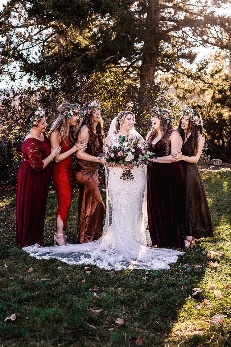 Bride centered between bridal party wearing reds and maroons and beautiful flower crowns in Wentworth Inn wedding in Jackson NH by Lisa Smith Photography