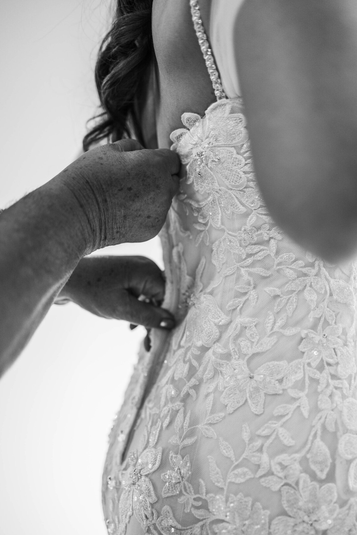 Details of a bride's dress being closed on her back with mom's help