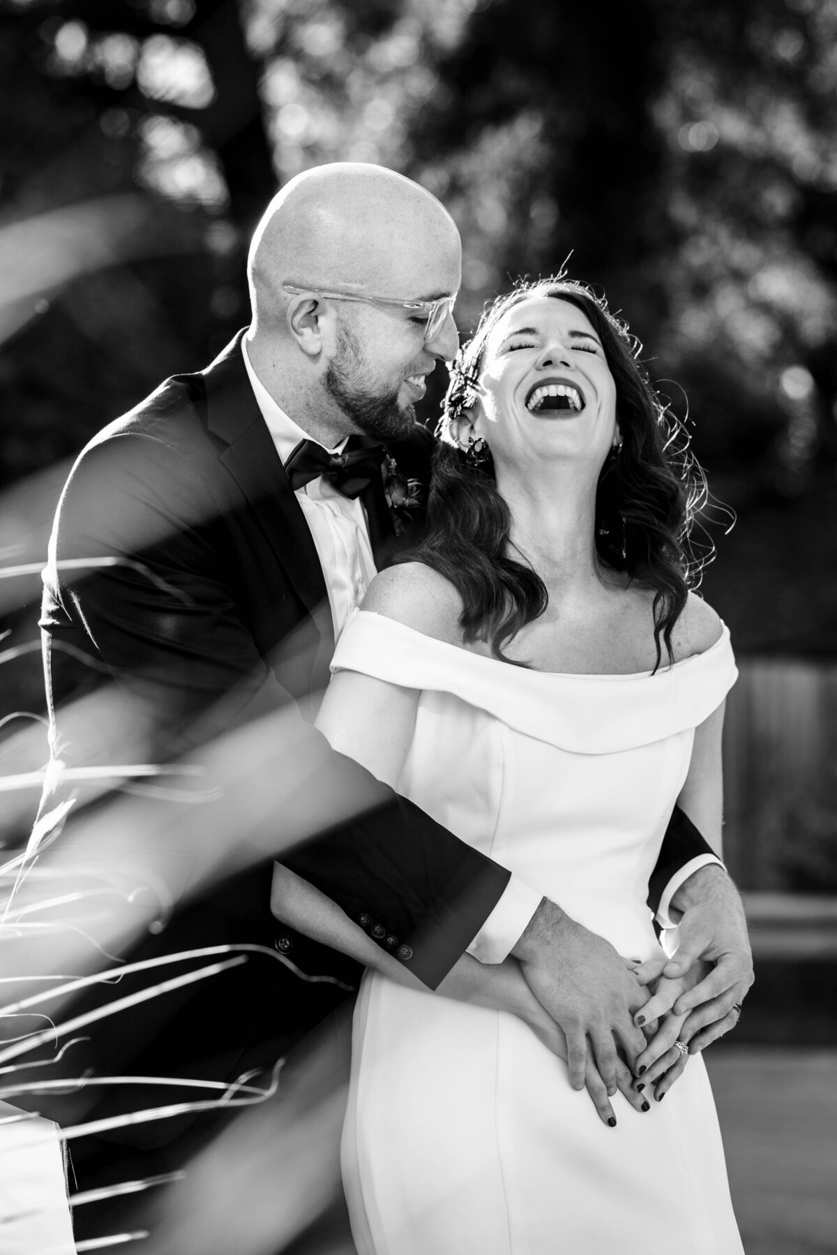 Black and white photograph of grooms arms around his bride from behind smiling at her as she leans her head back laughing by Charlotte wedding photographers DeLong Photography