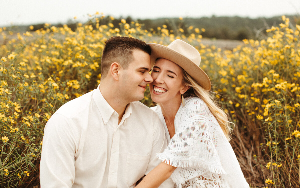 Bride and groom smiling and sitting in front of yellow flowers