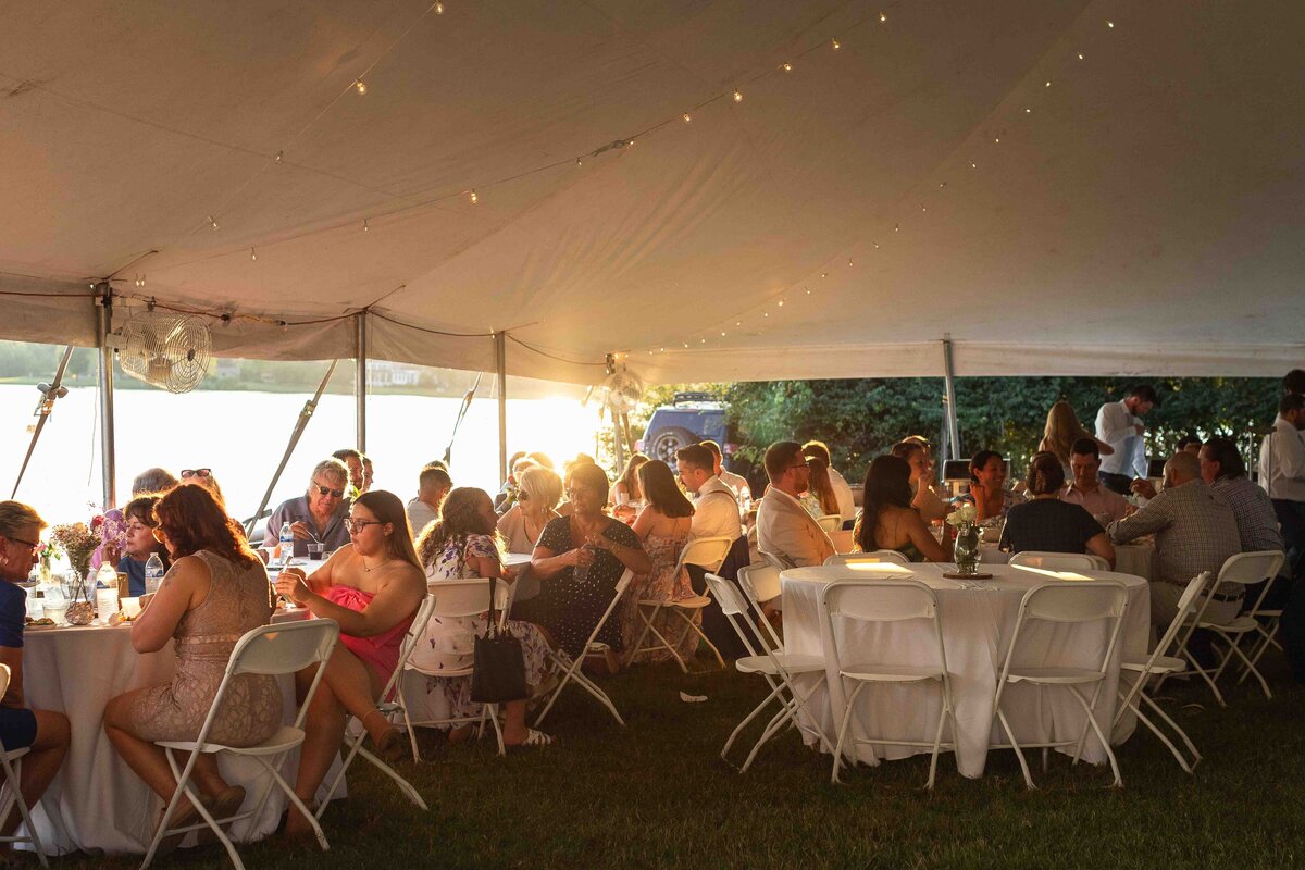 Wedding guests eating dinner at wedding reception outside during sunset