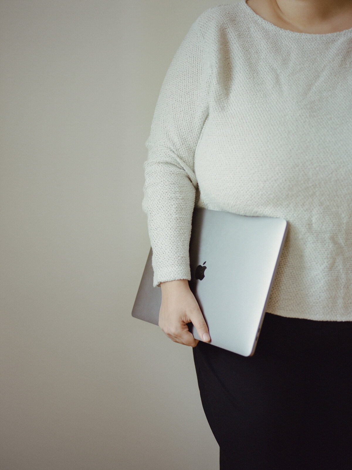 woman in white sweater holds folded macbook, clean white background, ALEO Detroit branding photoshoot
