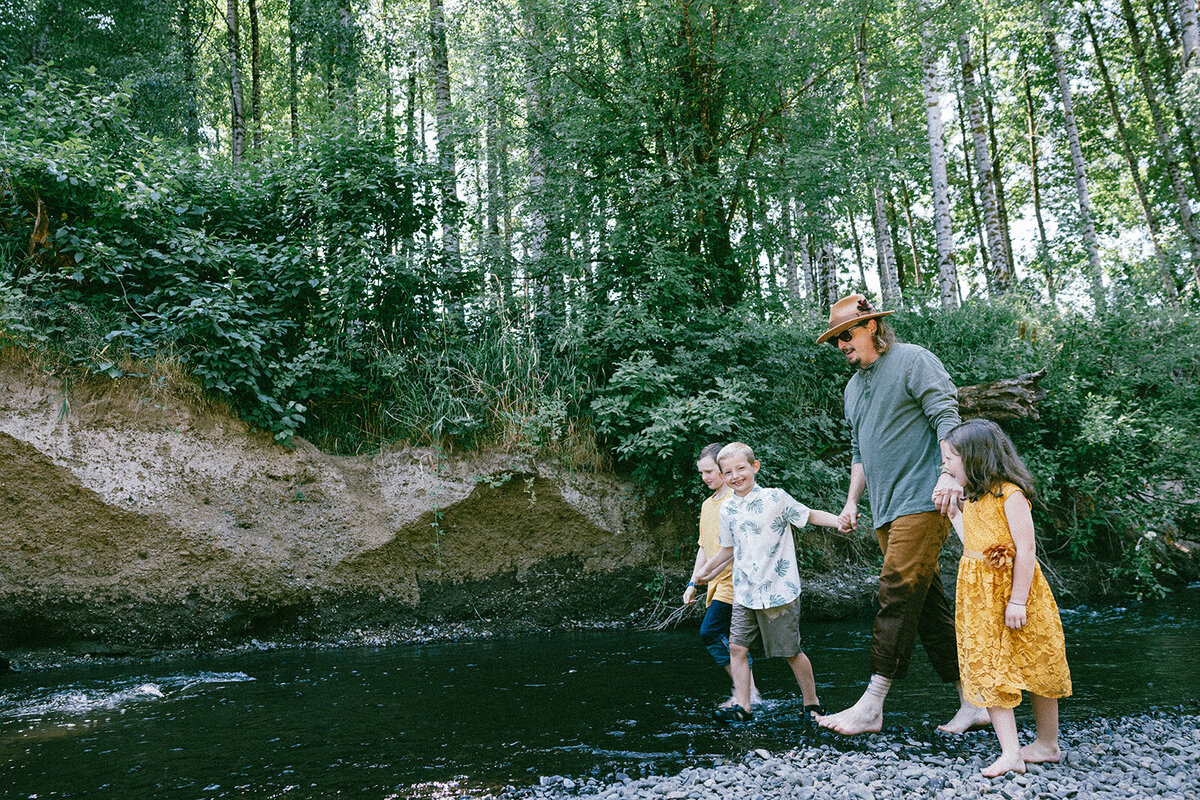 Family holds hands while wading in through the river in Oregon. 