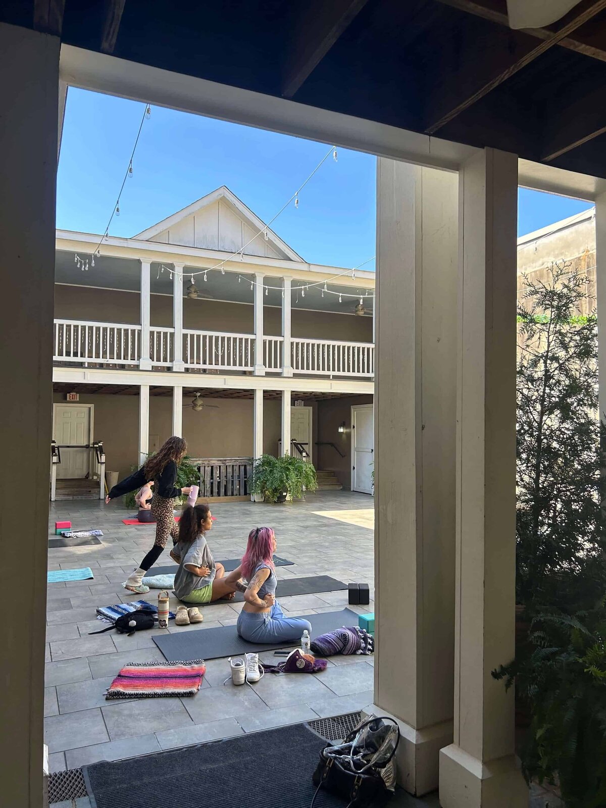 A group of women get set up for a yoga event in a brightly lit courtyard.