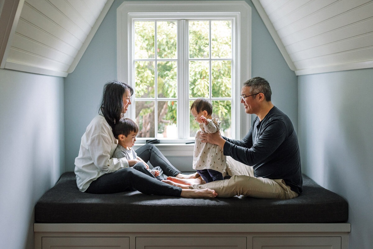 mom and dad and young children sitting in a window seat at home interacting and playing with each other