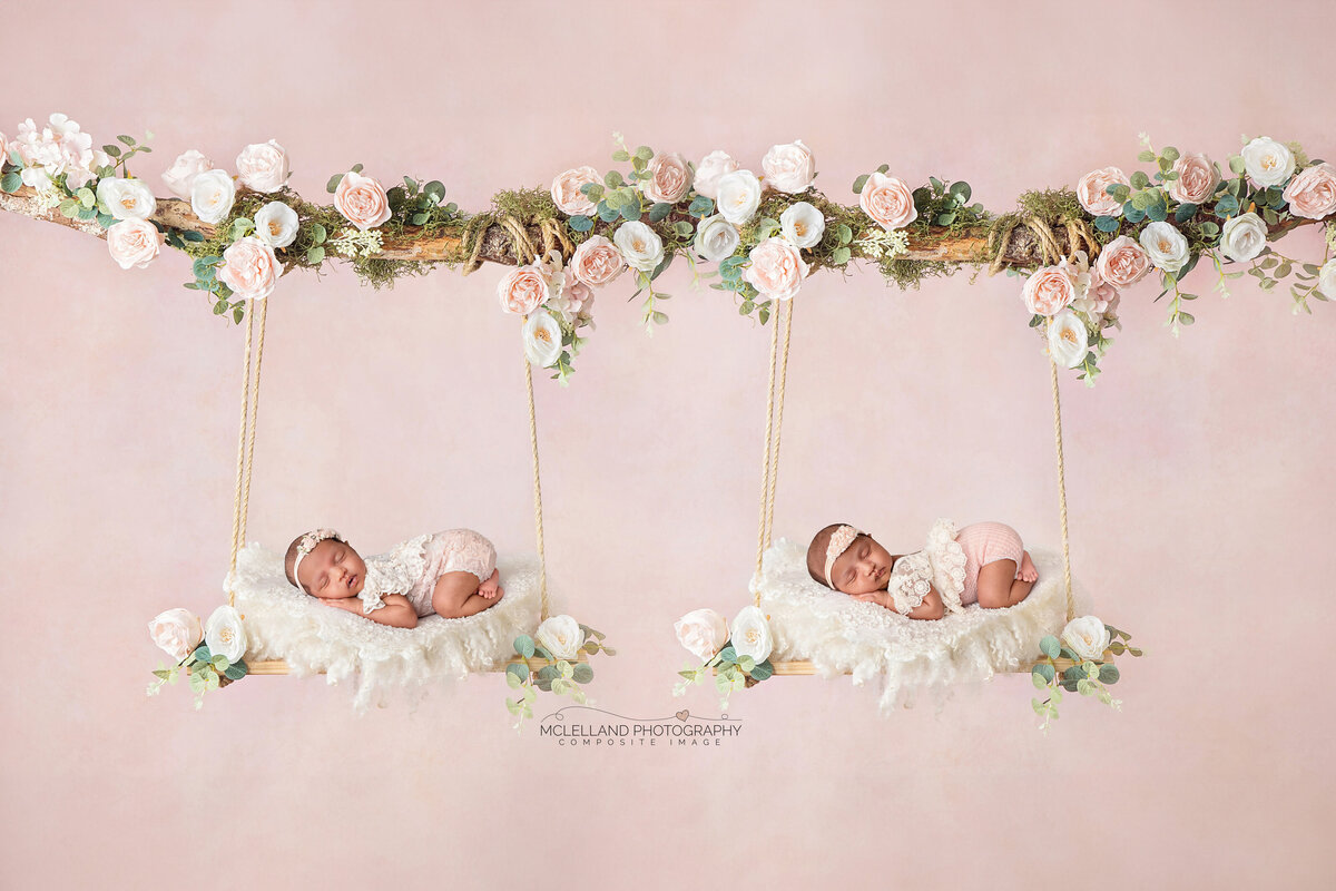 Newborn twin babies posed in matching swings decorated with white flowers and greenery.