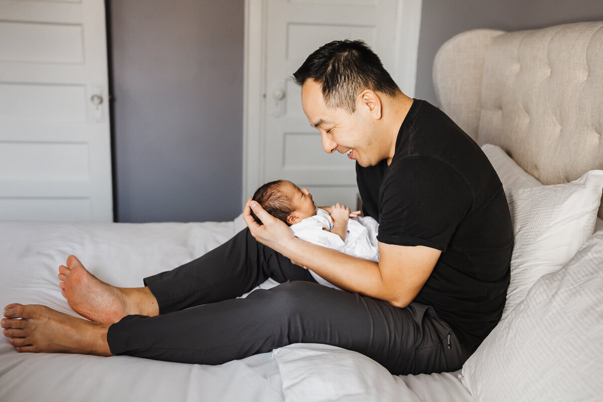Father sitting on bed holding newborn son