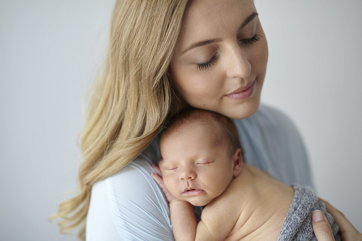 Content mum with eyes closed holding sleeping, newborn baby up on her chest