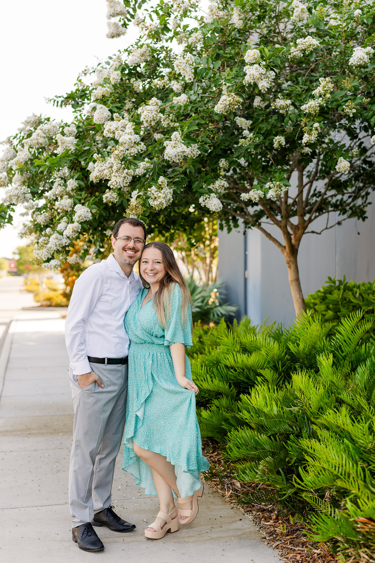 Husband and wife wedding photographers take portrait together in front of white floral tree