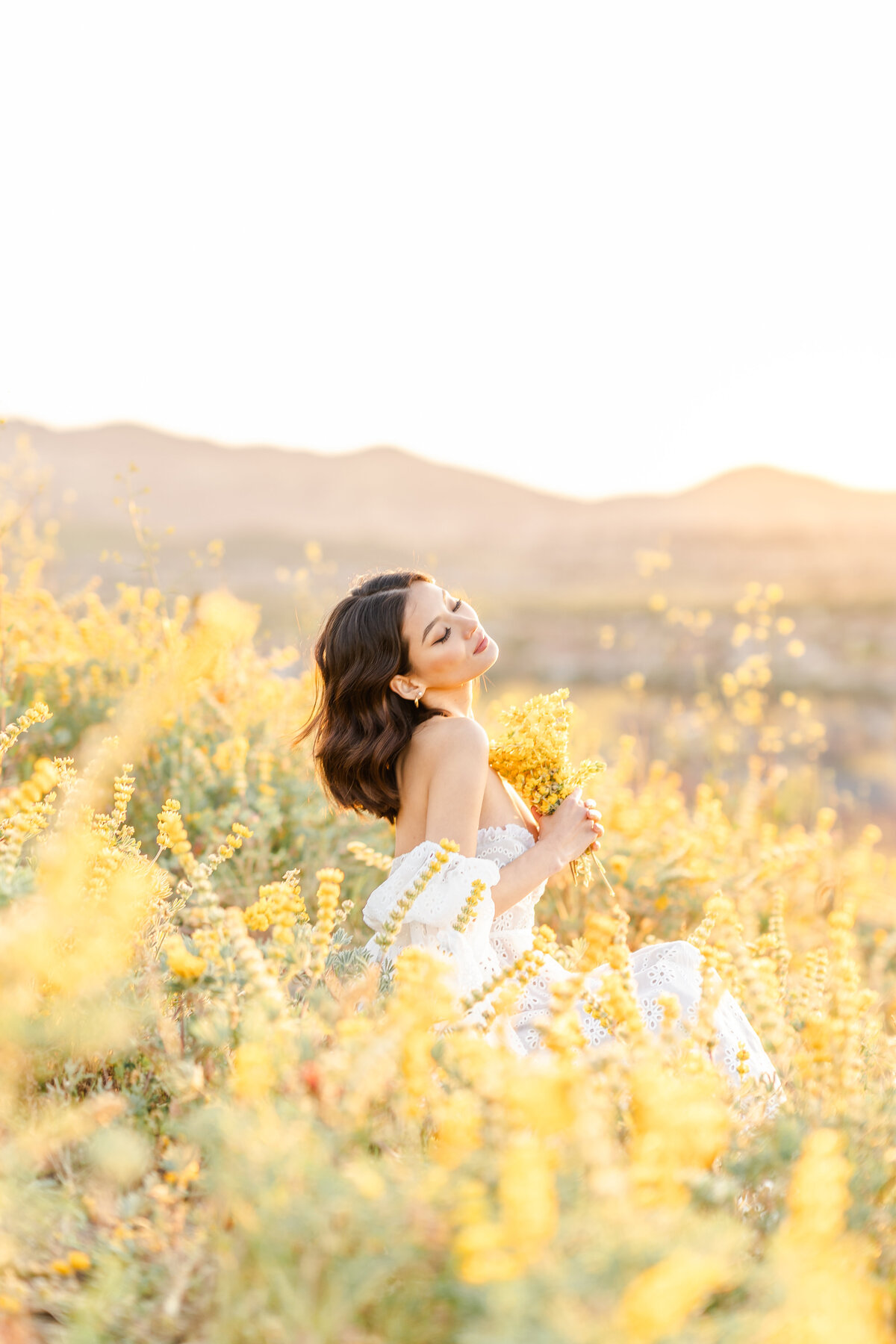 A woman sits in a field of yellow lupines while holding a bouquet of that flower photographed by Bay area photographer, Light Livin Photography.