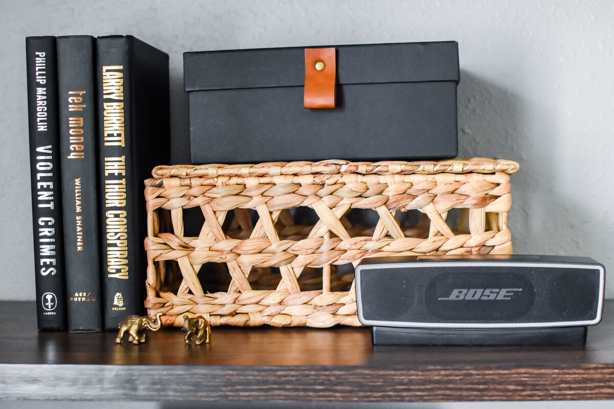 A black decorative box with a leather strap sits on top of a wicker box on a shelf