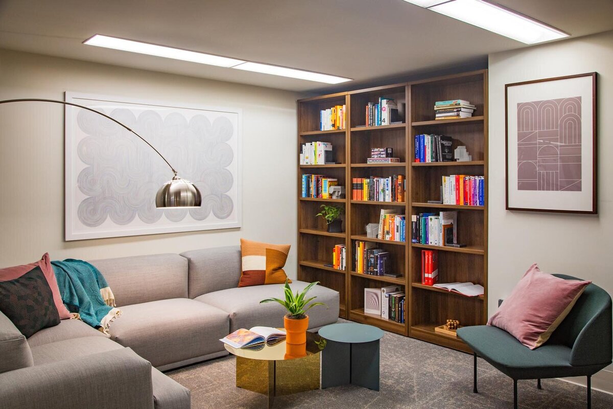 Library lounge with gray sectional, green armchair, and full wall of bookshelves filled with books and decor.