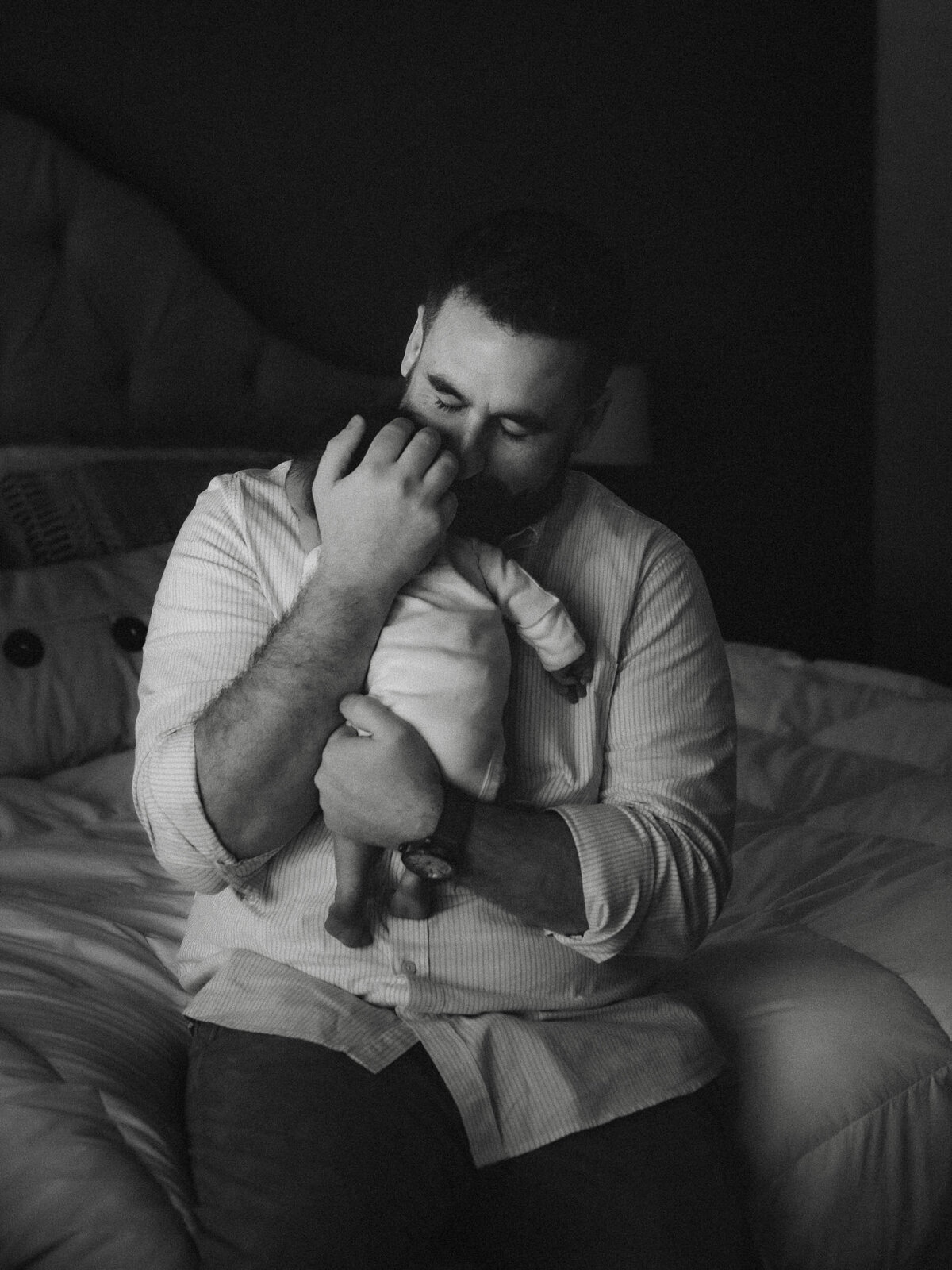 Black and white newborn portrait of a dad cradling his baby in dramatic light.