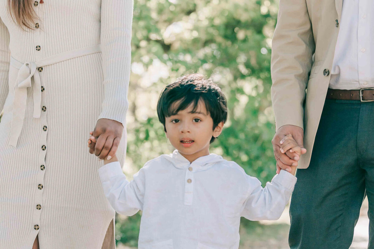 A close up of the young boy holding the hands of his parents. 