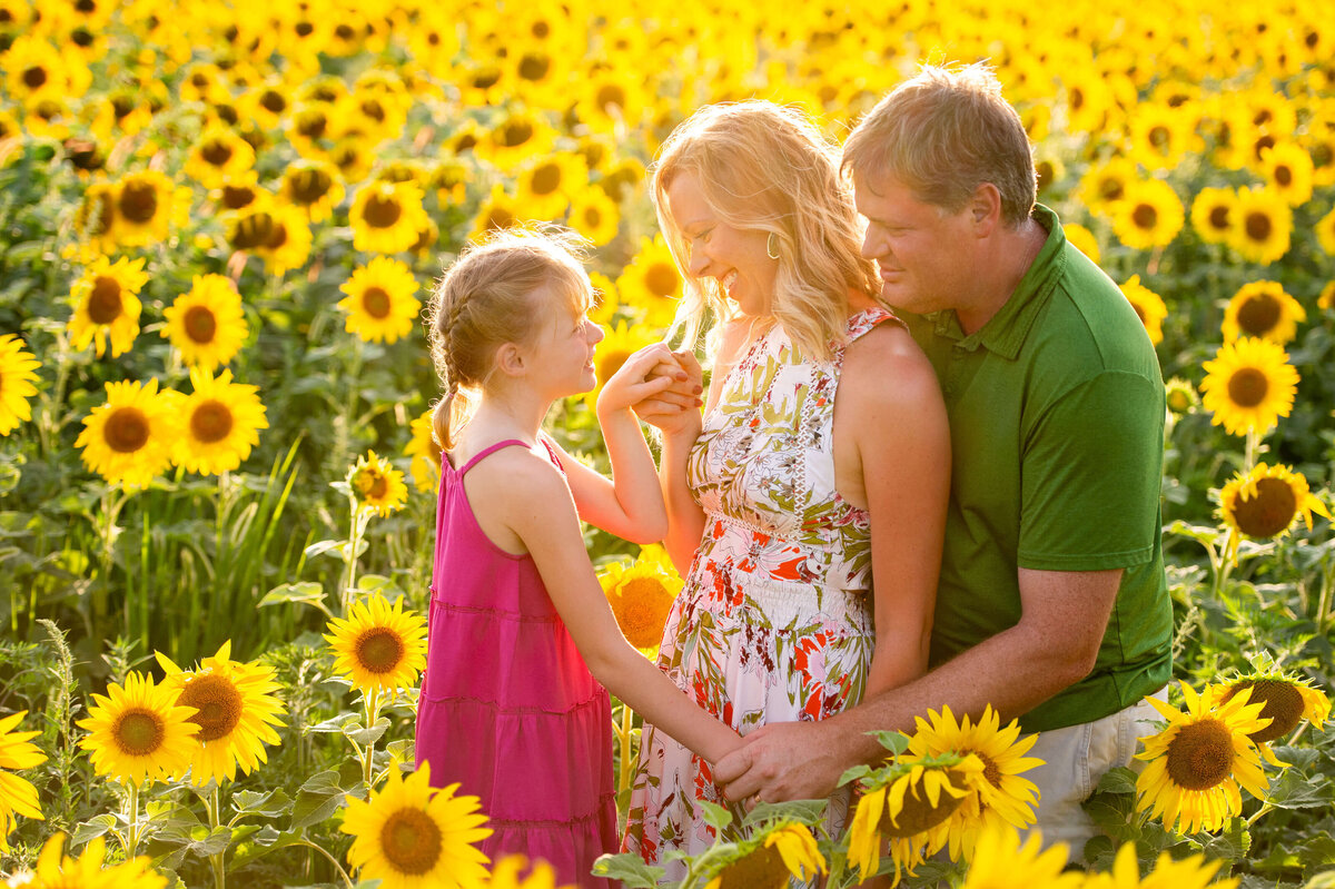 Ottawa family photography showing a mom, dad and little girl in a field of sunflowers taken at sunset