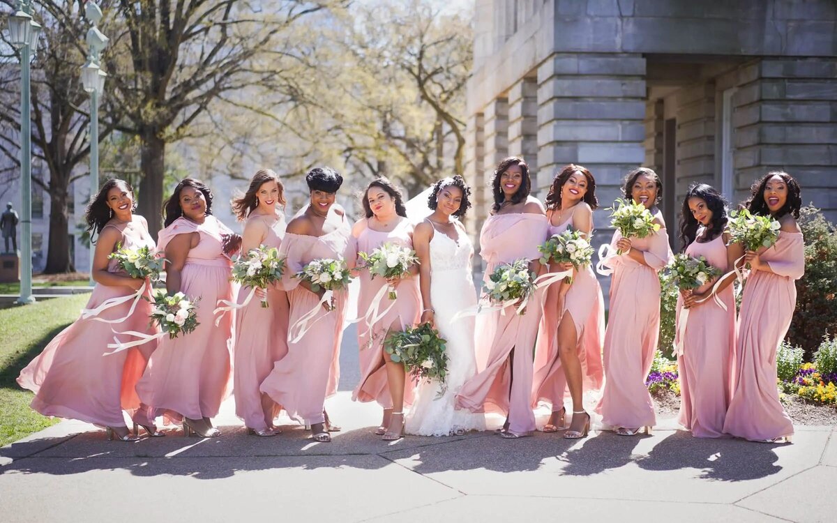 A bride leads her bridesmaids down a city street, their pink dresses and bouquets adding a splash of color to the urban landscape.