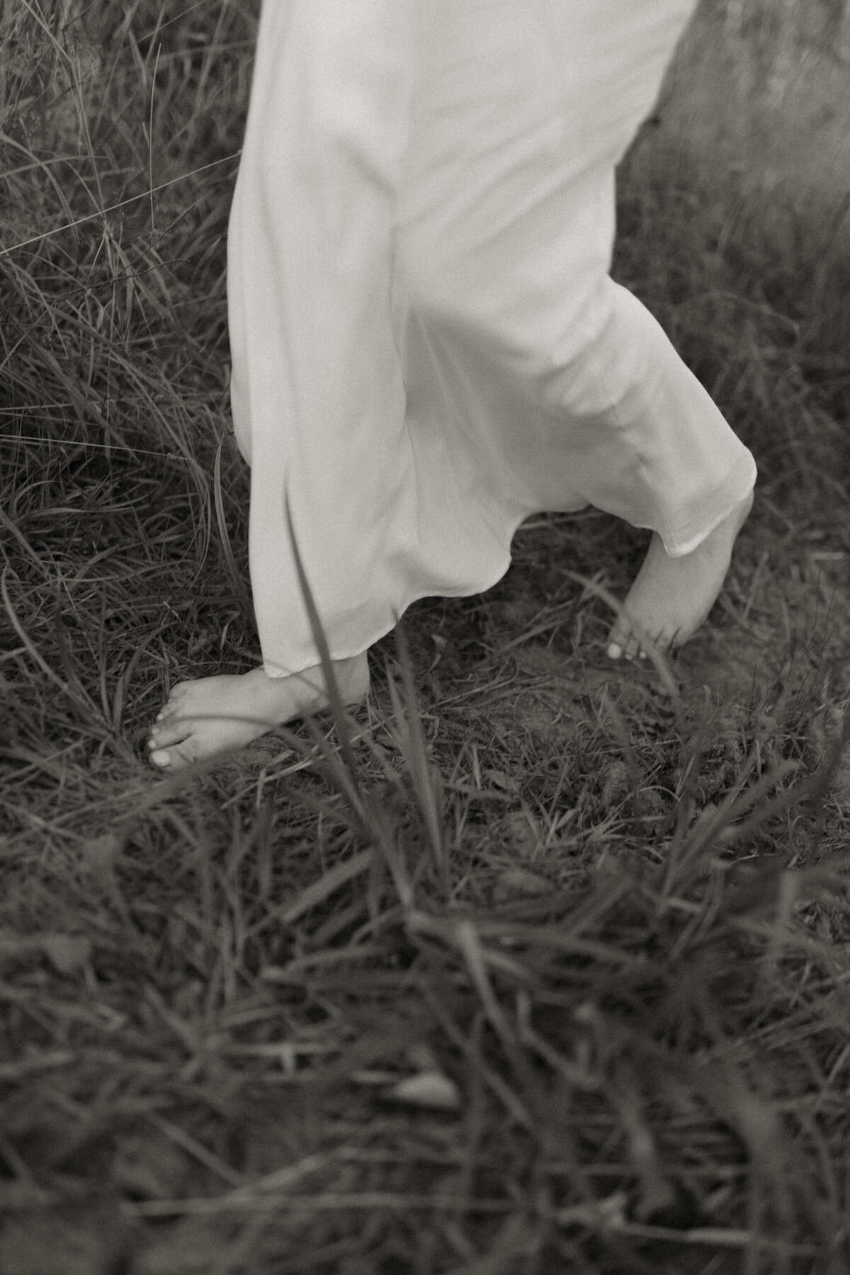 A bride-to-be strolls barefoot through the tall beach grass along Minnesota Point during a Twin Harbors engagement session in Minnesota.