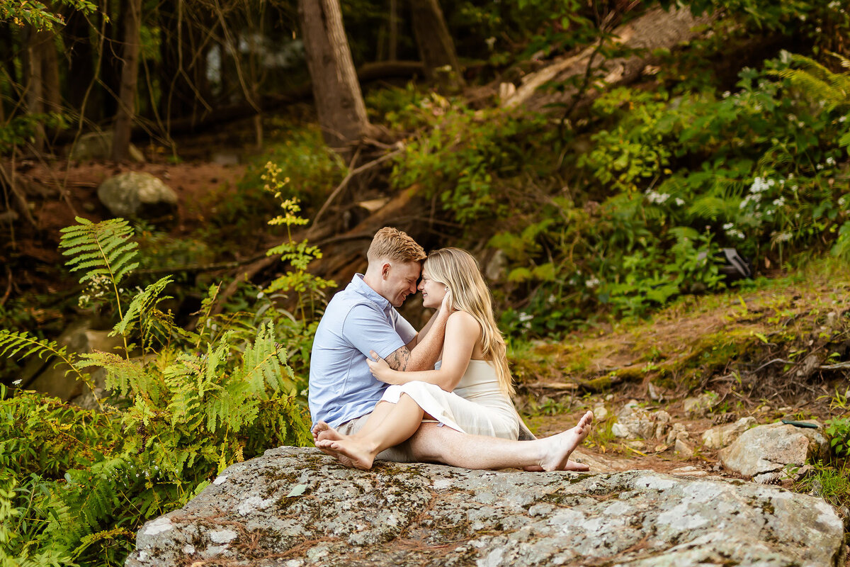 Couple sitting on rock and looking into each other eyes by nh engagement photographer lisa smith photography