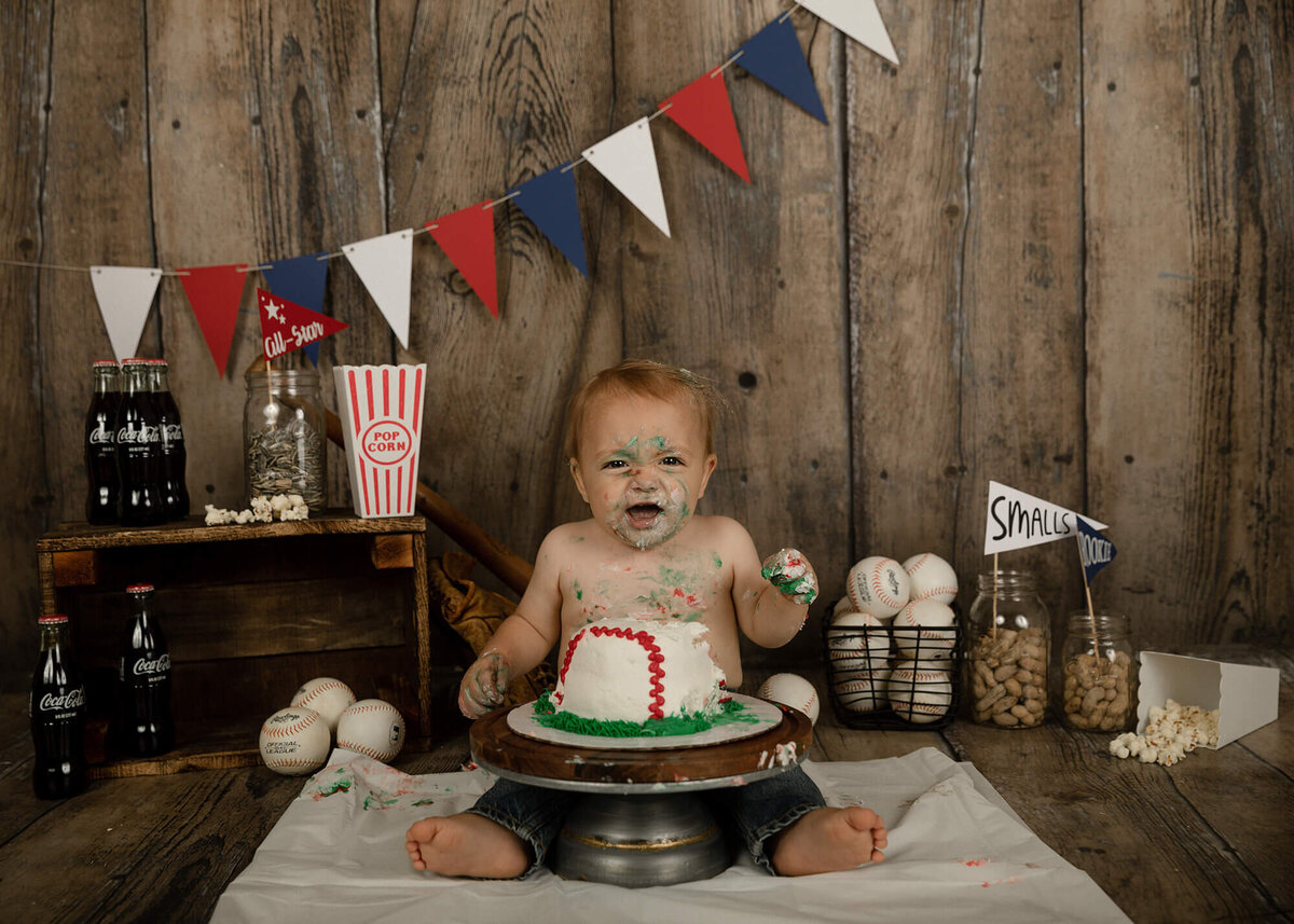 1 year old boy eating his baseball cake. Baseball themed decorations in the background.