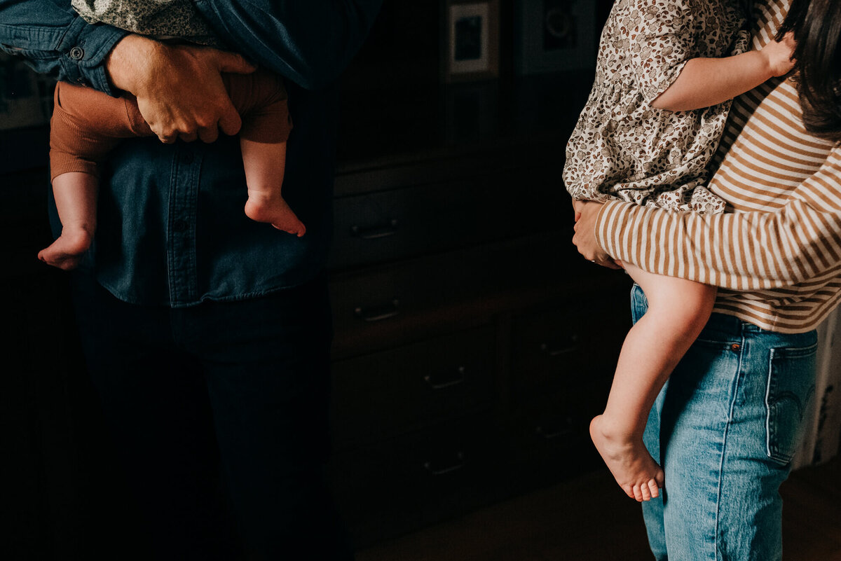 A close up image of a mother and father standing in their kitchen and holding their two young daughters