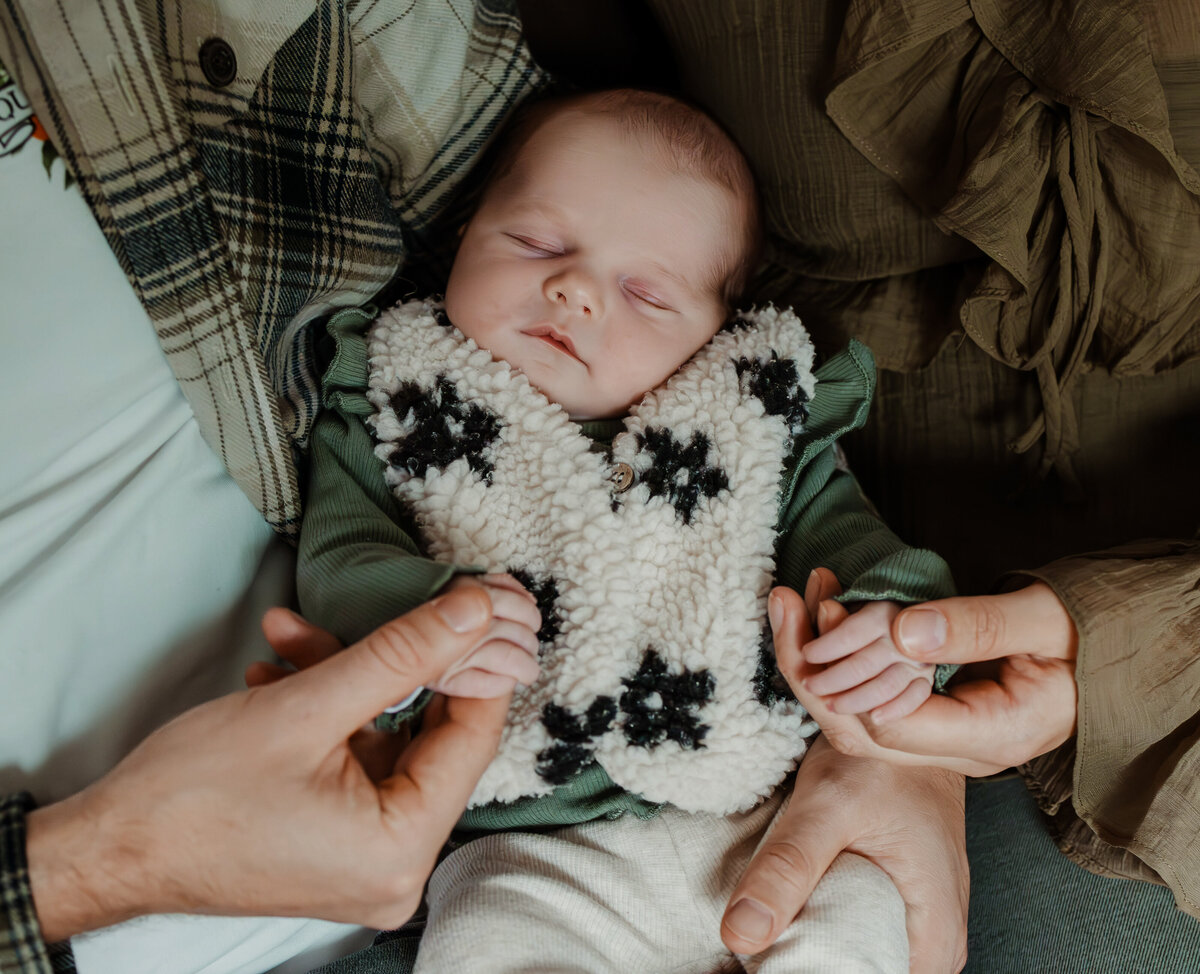 baby ligt op schoot bij papa en mama en papa en mama houden ieder een handje van de baby vast