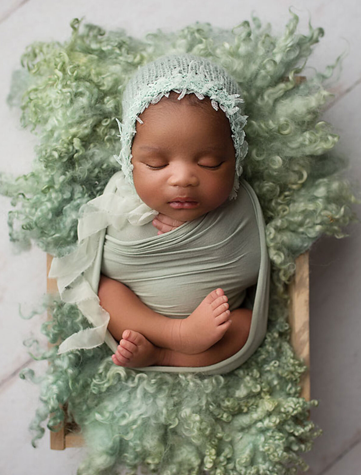 baby girl wrapped in a sage colored wrap and posed on a sage rug