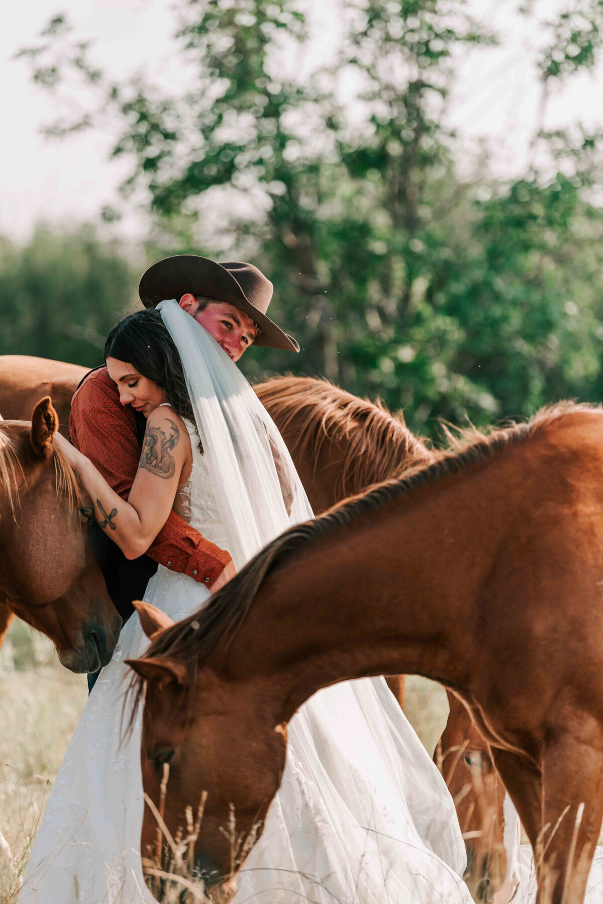 The bride goes in for a hug and leans on the grooms shoukder. The horses are around. 
