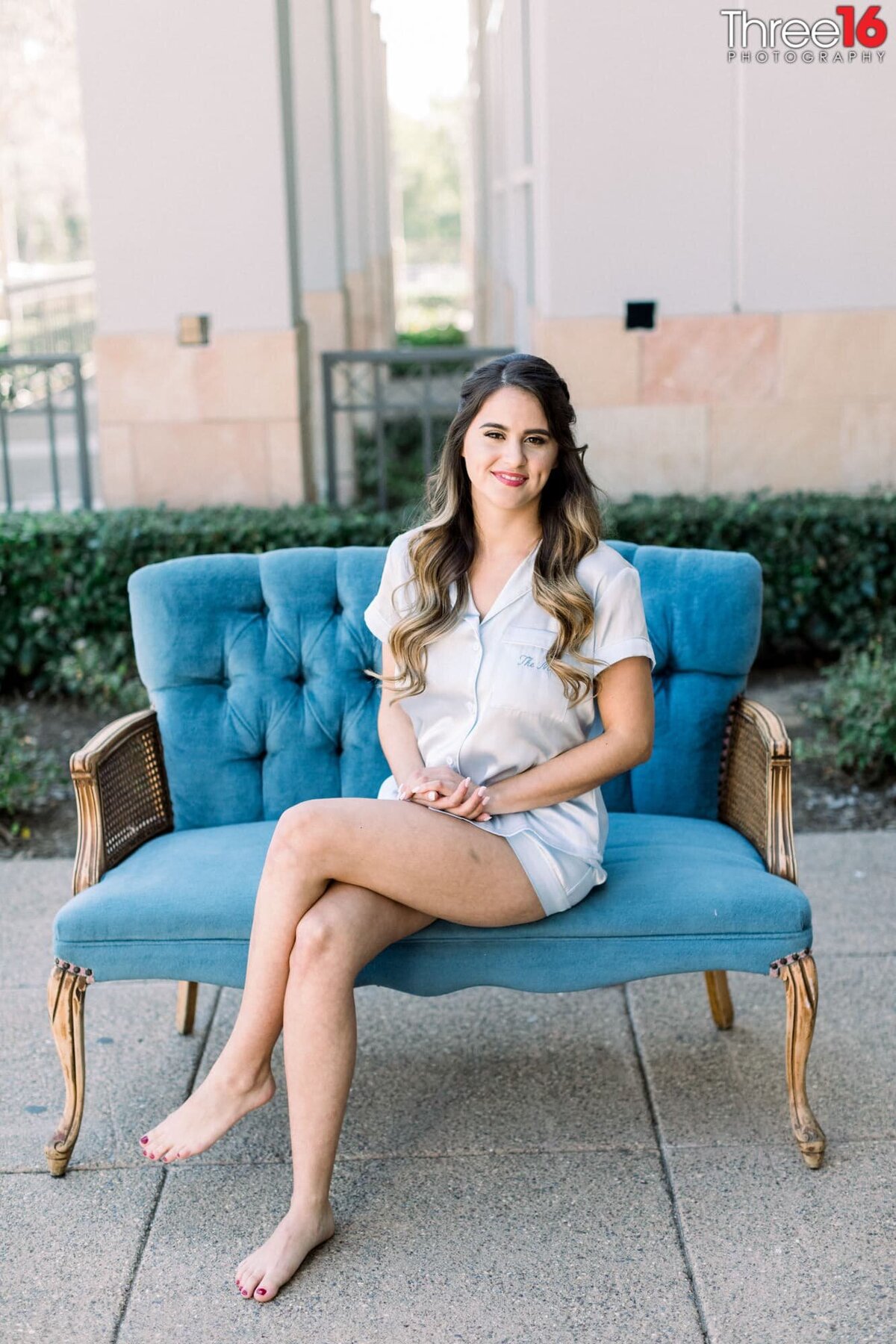 Bride sits on an antique love seat posing in her pre-wedding outfit