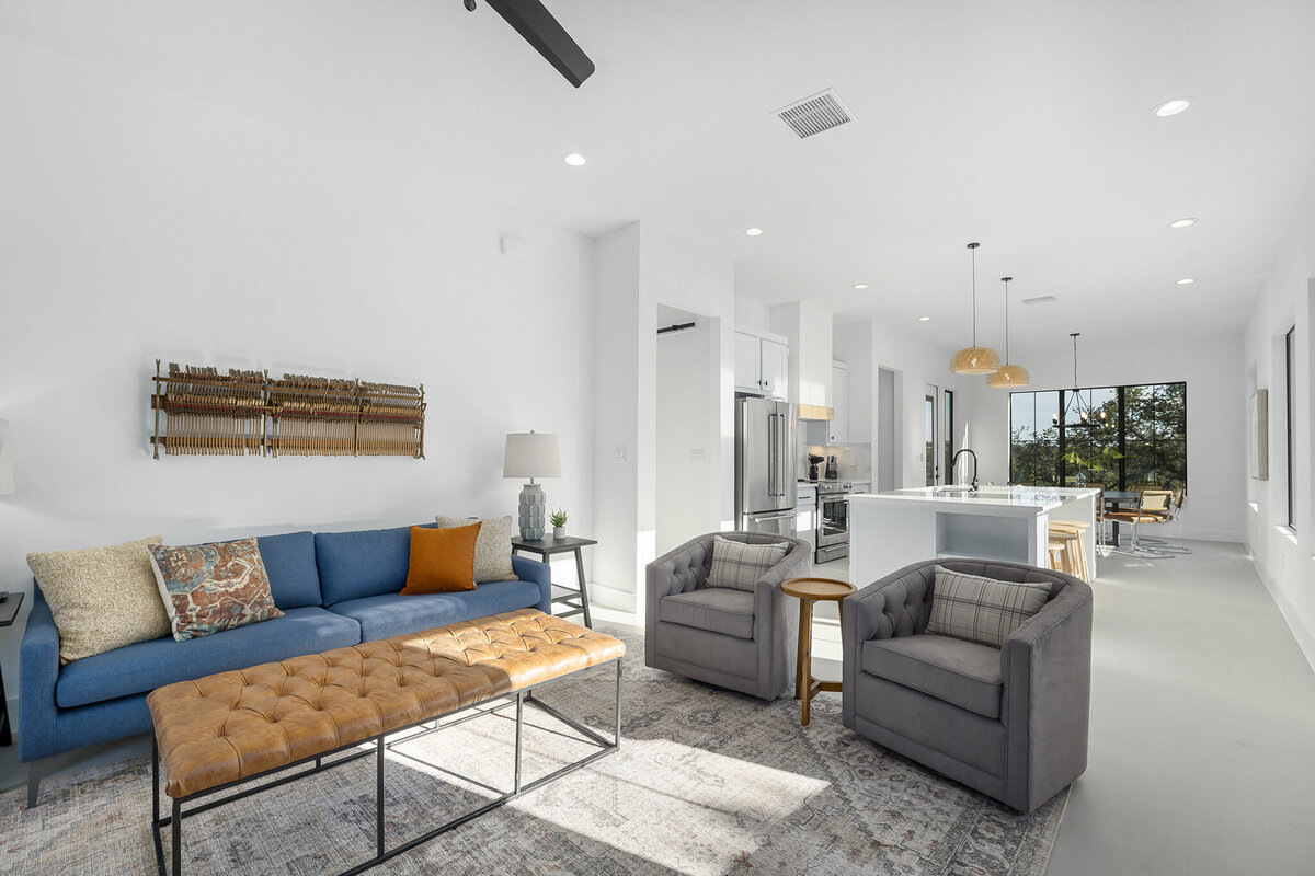 living room with blue couch, gray chairs and leather coffee tables open to kitchen