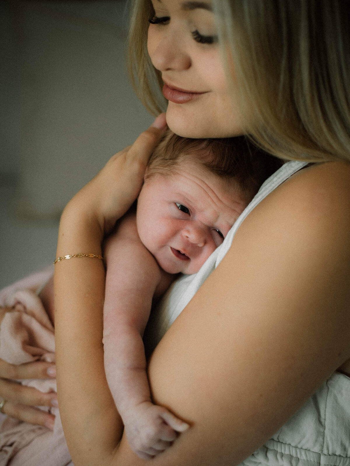Emotional lifestyle photo of a mother holding her newborn under her chin with gentle window light.