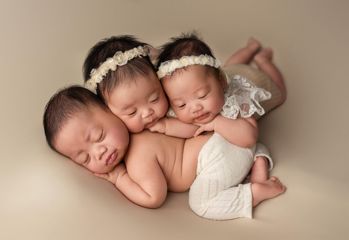 In studio Toronto newborn triplet portrait session of babies cuddled posed on top of eachother sleeping.