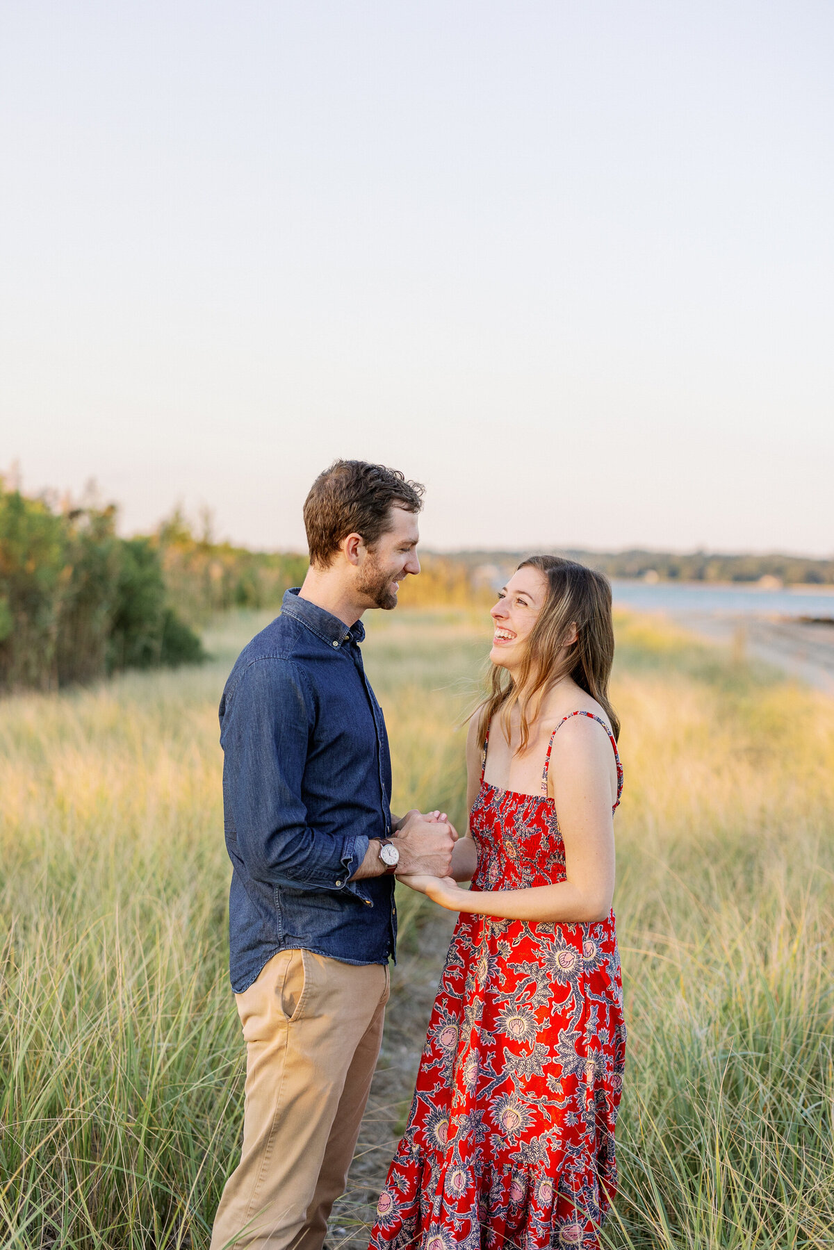 Couple standing in a field smiling as they hold hands.