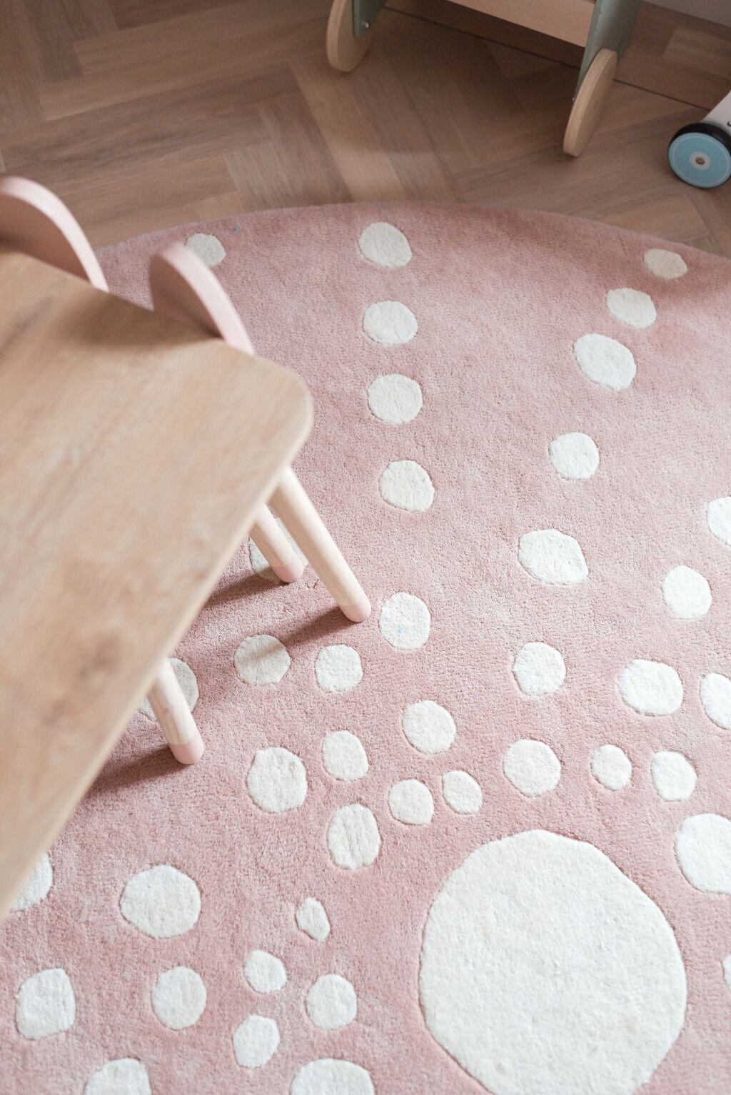 A close-up of a pink round rug with white polka dots of varying sizes, sitting on a light wooden floor.