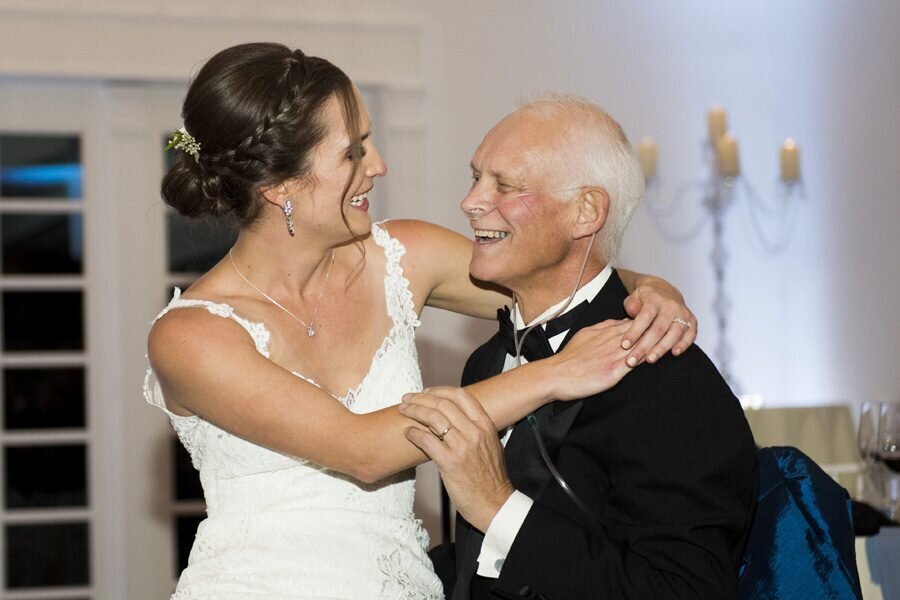 A bride wraps her hands around her father's neck as they smile at each other and share a dance during the wedding reception.